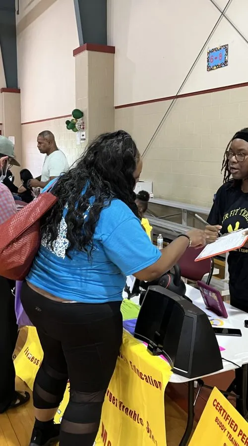 Una mujer con playera azul se registra en una mesa de recursos durante un evento comunitario