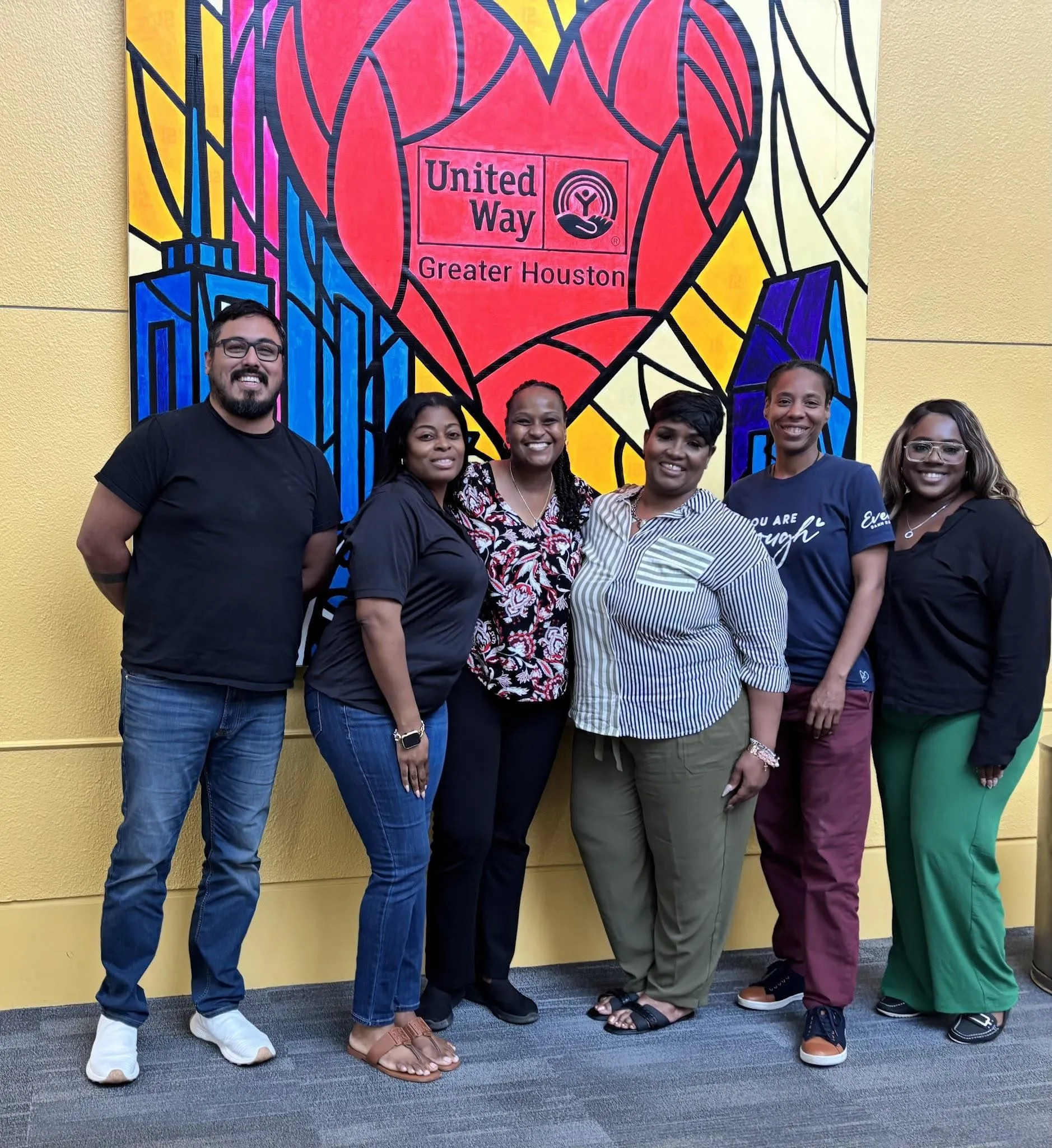 Seis integrantes de la red de Houston Peer Success sonriendo juntos frente al mural del corazón de United Way of Greater Houston
